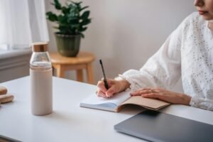 Adult writing in a notebook at a desk, stylish pen and minimalist setup.